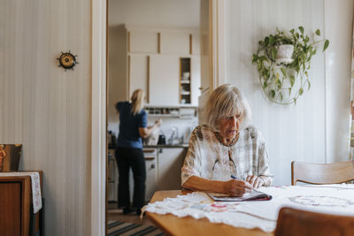 Senior woman doing puzzle in book while sitting at dining table in home