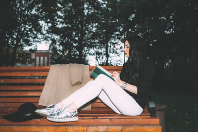 Young woman sitting on bench with book