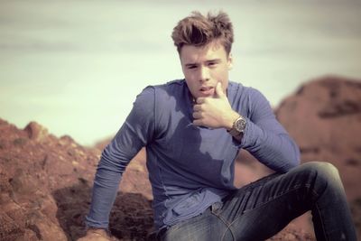 Portrait of young man sitting on landscape against sky