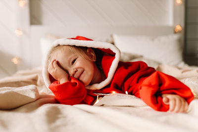 A funny happy little girl child in red pajamas is lying having fun on bed in a decorated cozy house