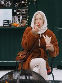 Young woman with blonde hair wearing brown fur coat eating sweet food on the christmas market. 