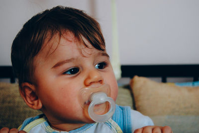 Close-up of baby boy with pacifier in mouth looking away at home