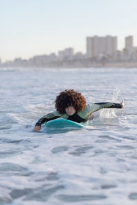 Young female surfer in wetsuit lying on waving seawater and enjoying summer day