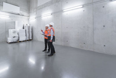 Two colleagues wearing safety vests and hard hats talking in a building
