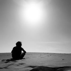 Man sitting on beach against clear sky