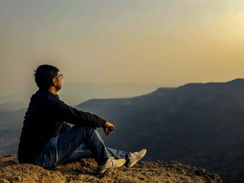 Side view of young man looking at mountain against sky