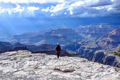 Rear view of woman standing on rocky mountain against cloudy sky