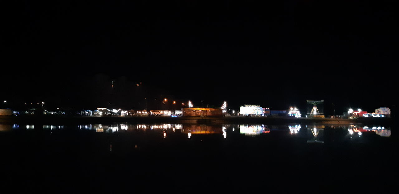 ILLUMINATED BUILDINGS BY RIVER AGAINST SKY