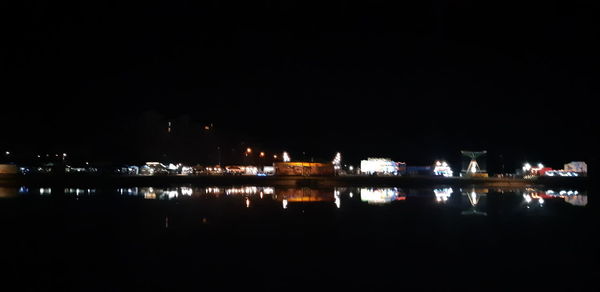 Illuminated buildings by river against sky at night