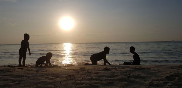 Silhouette dogs on beach against sky during sunset