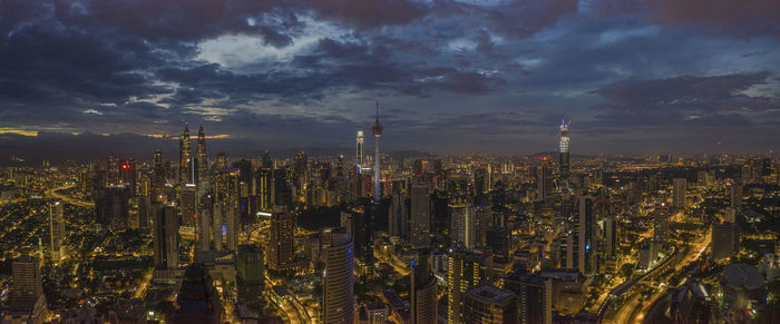 Aerial view of illuminated city against cloudy sky