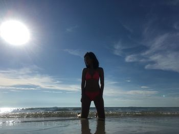 Woman kneeling on shore against sea at beach