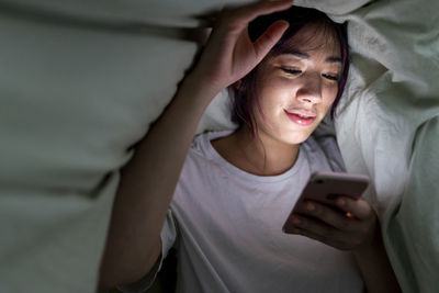Smiling woman using smart phone under blanket at home
