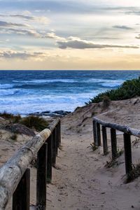 Wooden posts on beach against sky during sunset