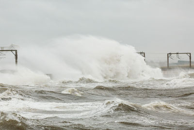 Storm waves crash against  a harbour on the west coast of scotland obscuring the lighthouse