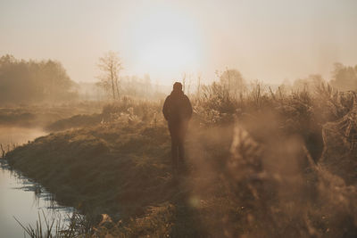 Rear view of silhouette man standing by lake against sky at sunrise