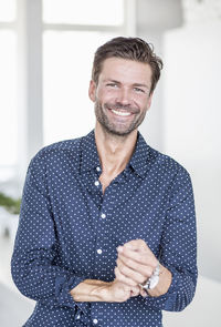 Portrait of happy businessman rolling up shirt sleeves in office