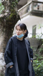 Young woman with flu mask looking away while standing in park