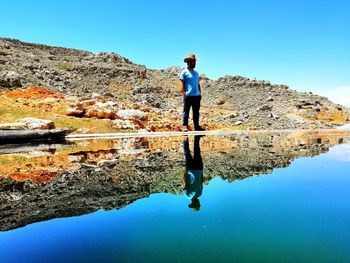 Man standing by lake against clear blue sky