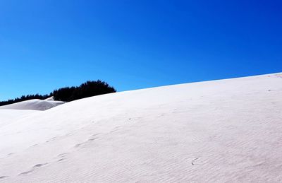 Low angle view of snow covered land against clear blue sky