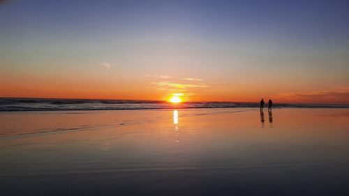 Lover couple walking on wet sand beach at sunset