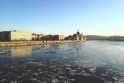 Sea by cityscape against clear sky