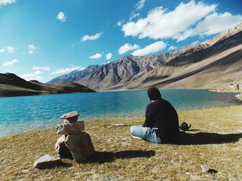 Rear view of man sitting on lakeshore