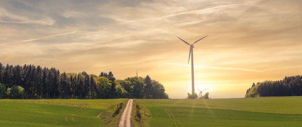 Scenic view of field and wind turbines against sky during sunset