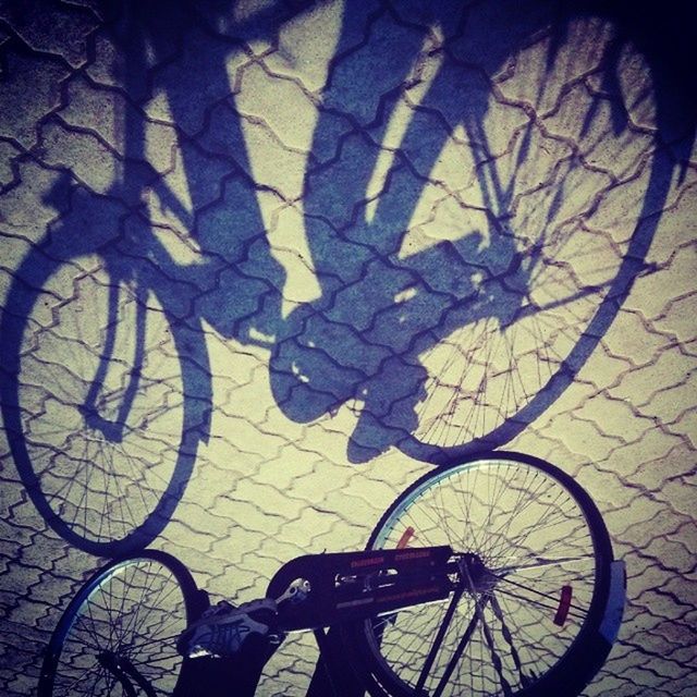 bicycle, transportation, land vehicle, mode of transport, shadow, street, sunlight, parking, stationary, high angle view, cycling, parked, road, outdoors, day, part of, no people, wheel, silhouette, travel