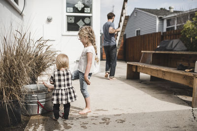 Girls playing with water in container outside house