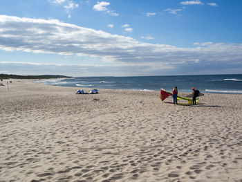 People standing at sandy beach against sky