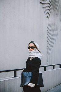 Portrait of woman wearing sunglasses standing against wall