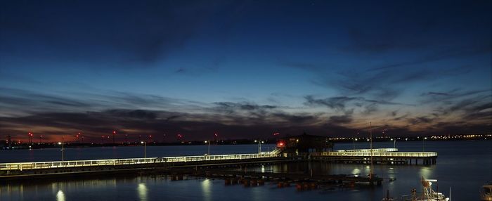 Illuminated pier over sea against sky at night