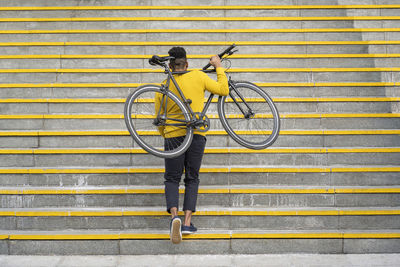 Young man carrying bicycle while climbing on staircase