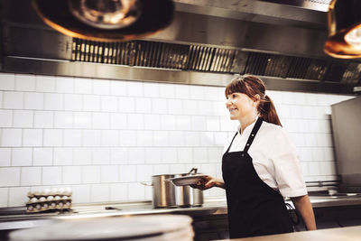 Female chef holding plate white walking in commercial kitchen