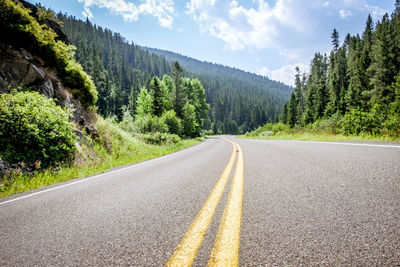 Empty road amidst trees against mountains