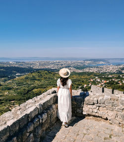 Rear view of woman standing on top of klis fortress overlooking coastal city of split in croatia.