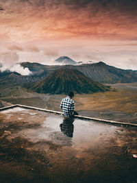 Reflection of man in puddle against mountain range