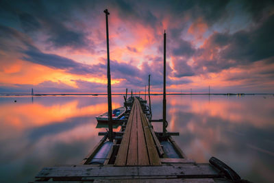 Low angle view of jetty in sea against sunset sky