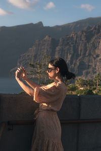 Woman looking at camera while standing on mountain against sky