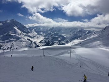 Tourists on snow covered mountain against cloudy sky