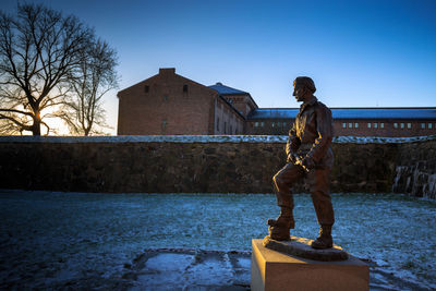 Statue of man standing by building against clear sky