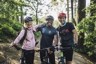 Portrait of happy male and female friends with cycles standing at footpath