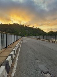 Road by footpath against sky during sunset