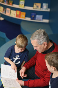 Grandfather reading to grandsons in library