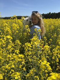Rear view of woman standing amidst yellow flowering plants on field