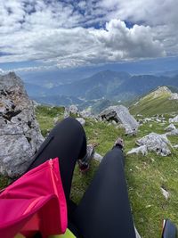 Low section of woman sitting on rock against sky