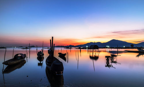 Boats moored in lake against sky during sunset