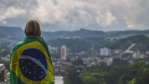 Rear view of woman wrapped in brazilian flag against sky