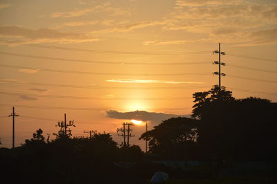 Silhouette trees and electricity pylon against romantic sky at sunset